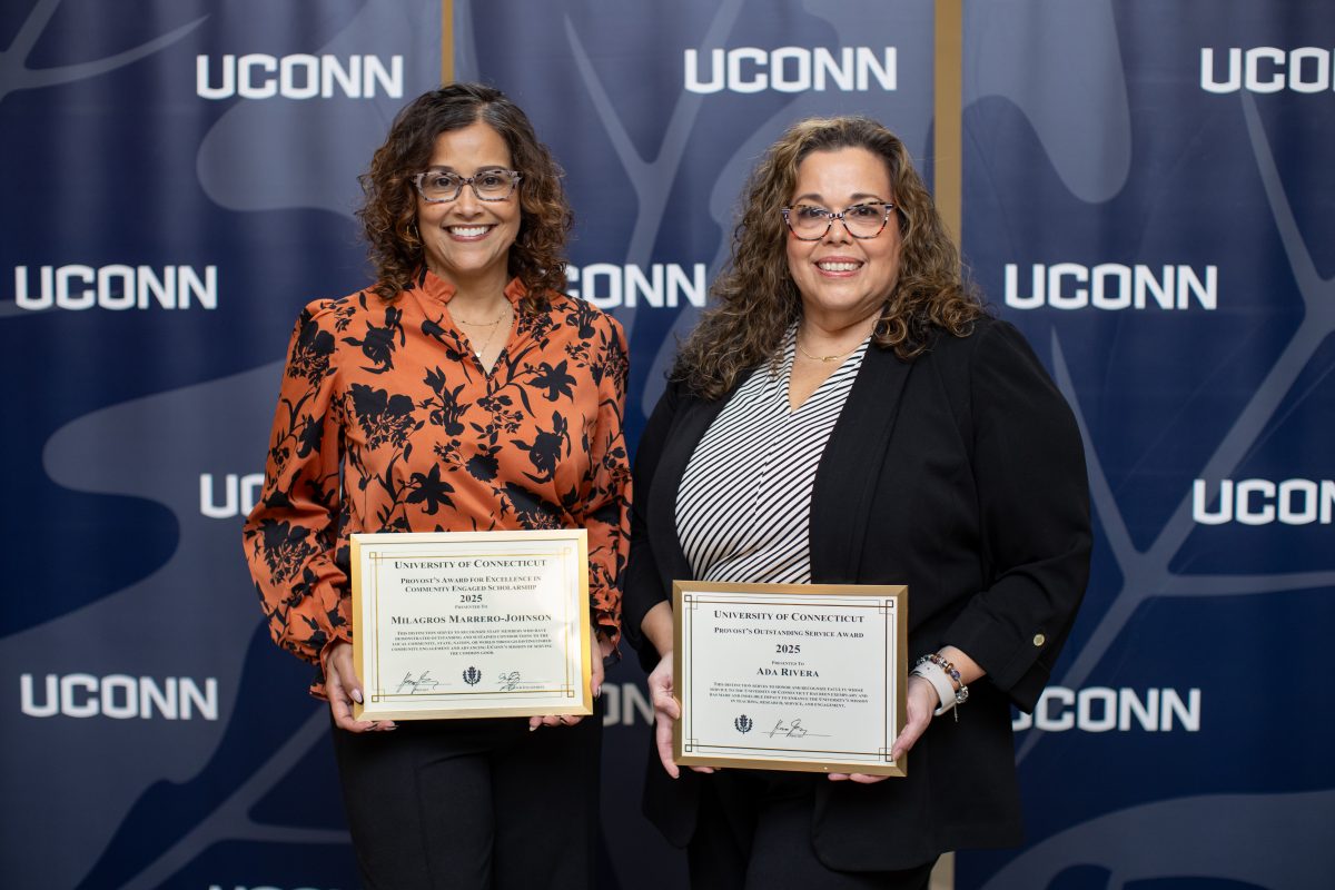 Two people posing for a picture in front of a UConn sign.