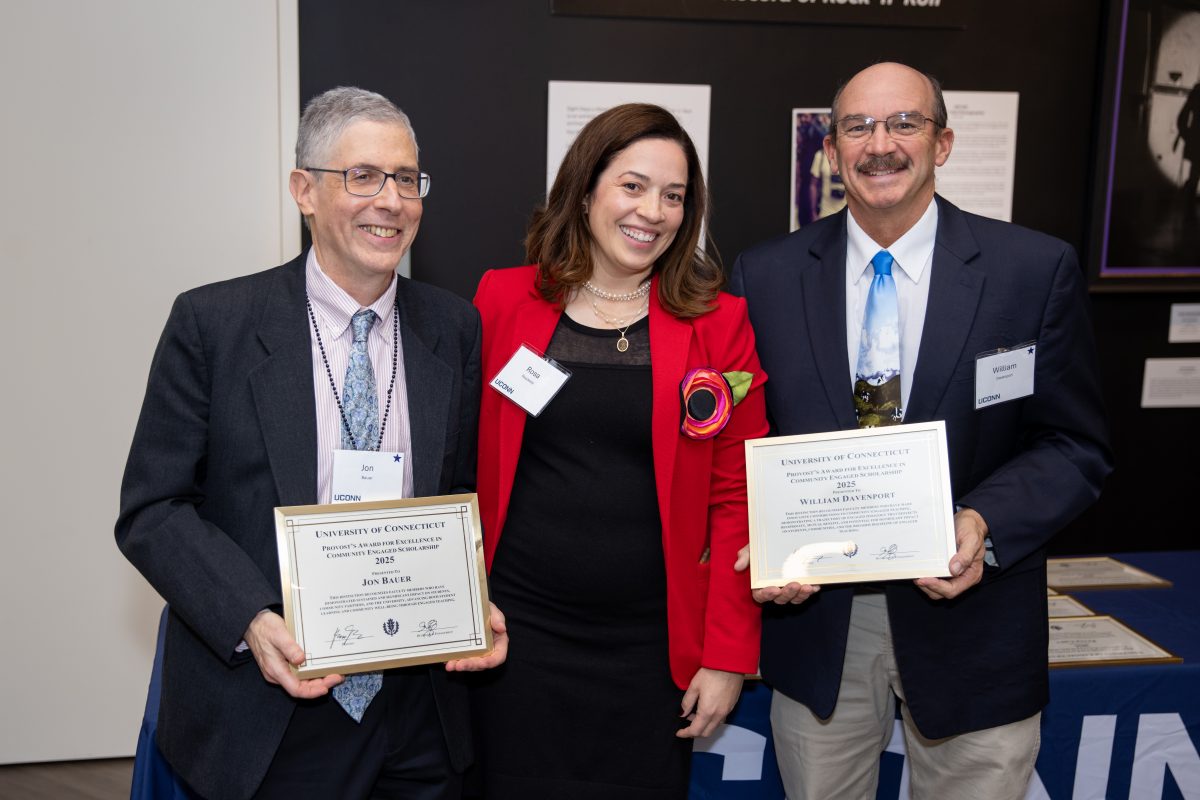 A group of people posing in front of a UConn sign.