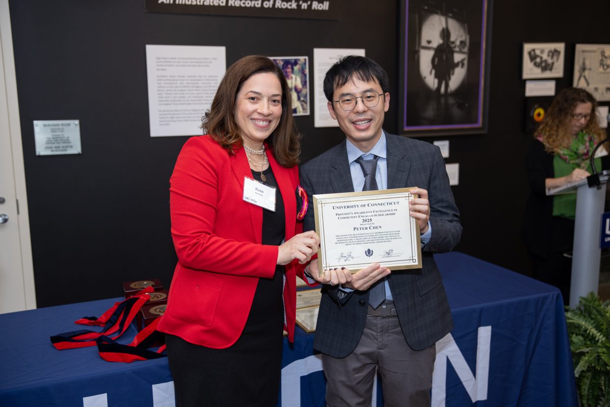 A group of people posing in front of a UConn sign.
