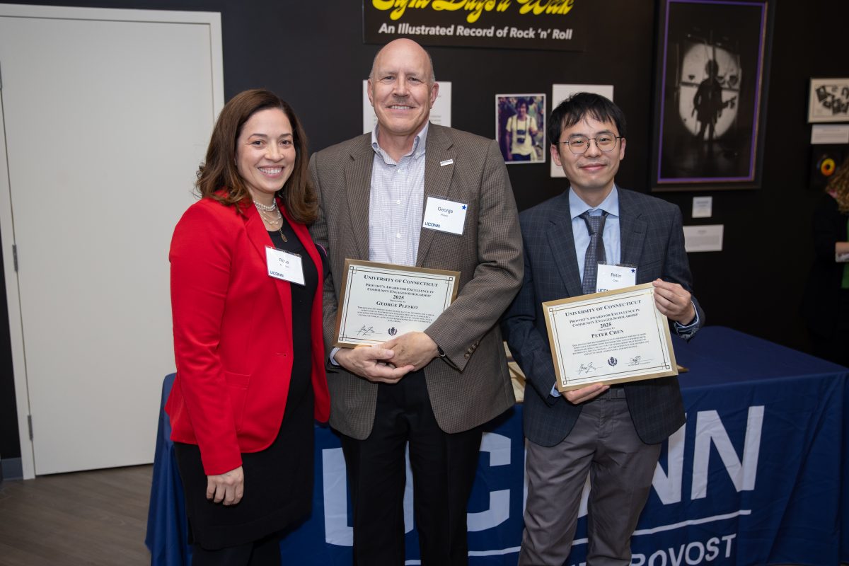 A group of people posing in front of a UConn sign.