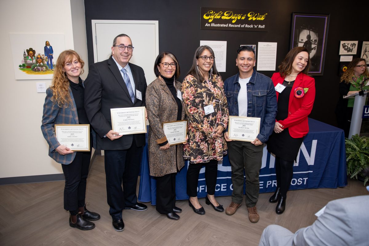 A group of people posing in front of a UConn sign.