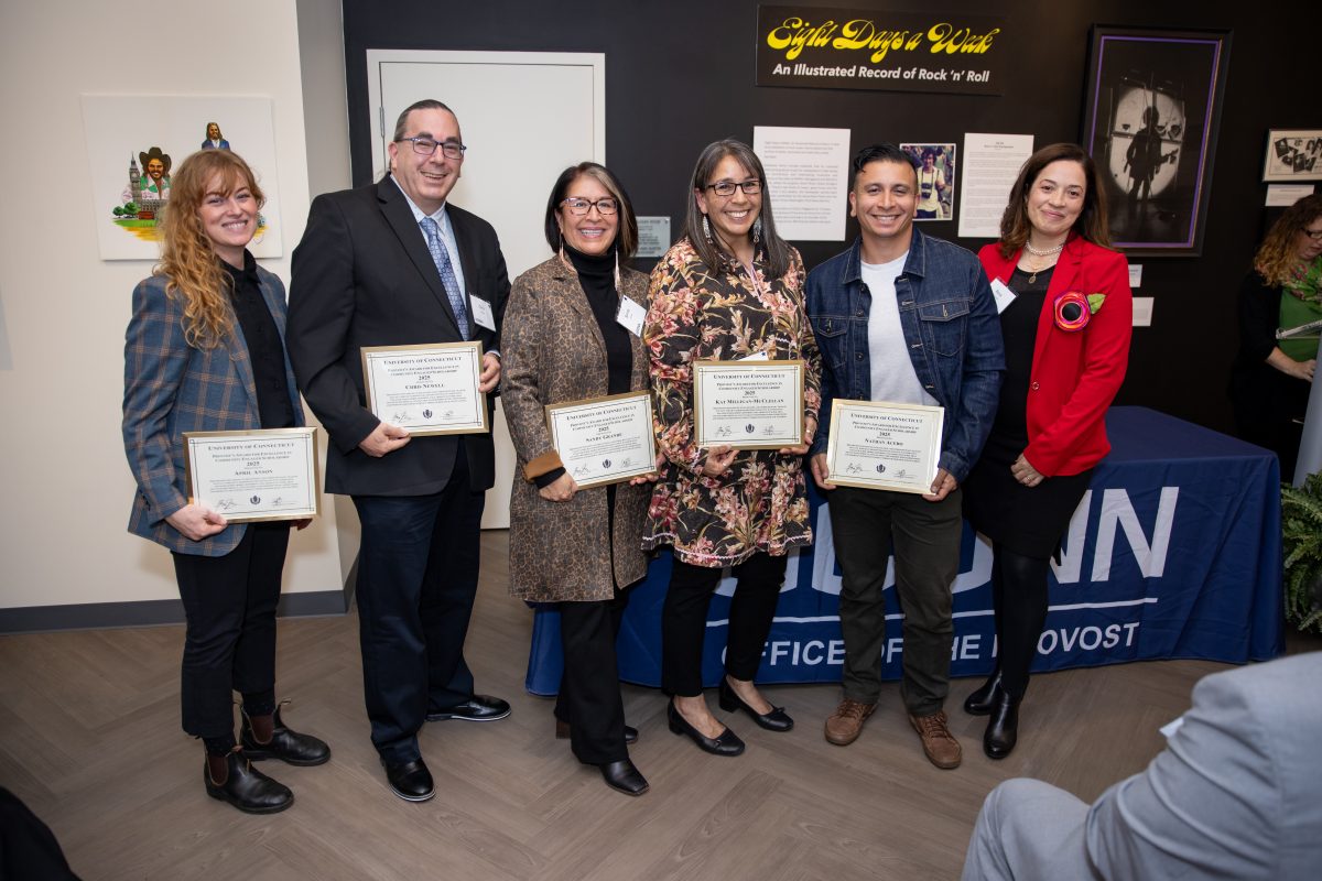 A group of people posing in front of a UConn sign.