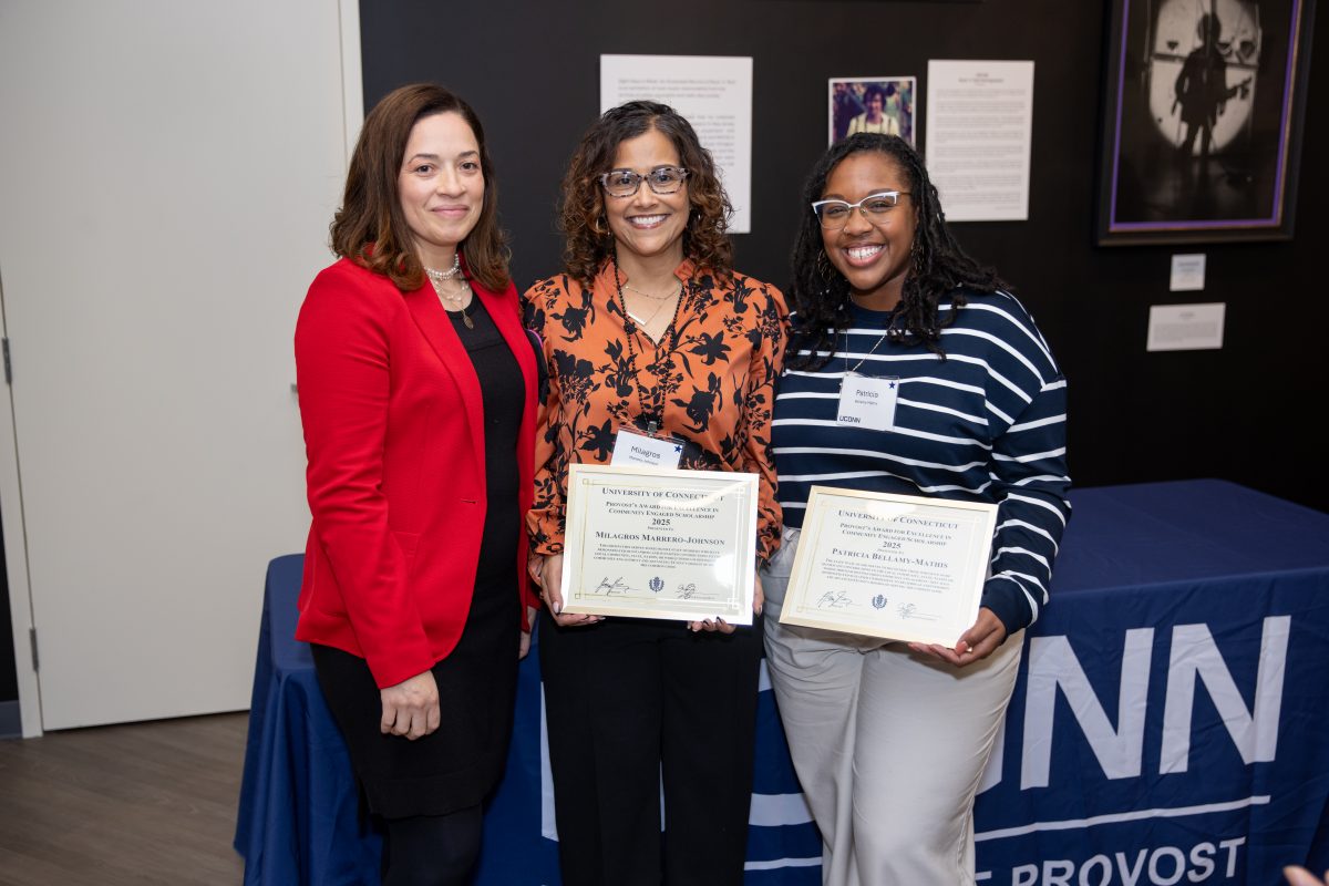 A group of people posing in front of a UConn sign.