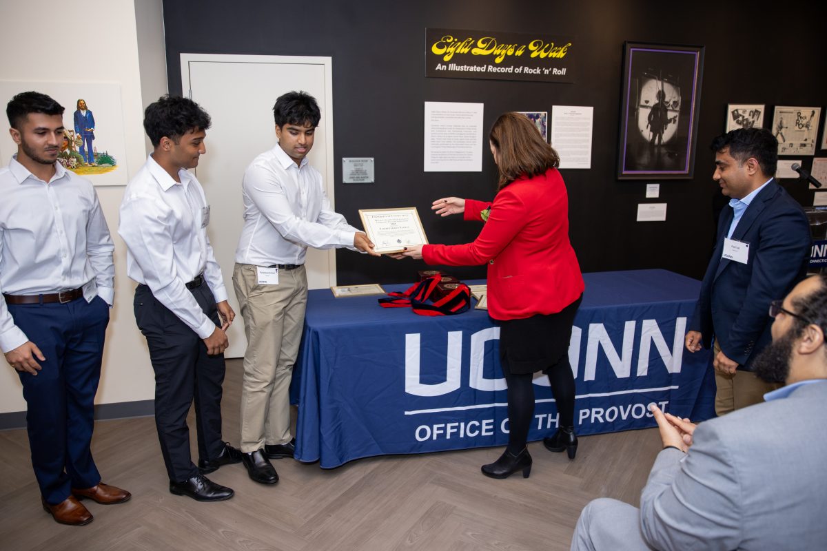 A group of people posing in front of a UConn sign.