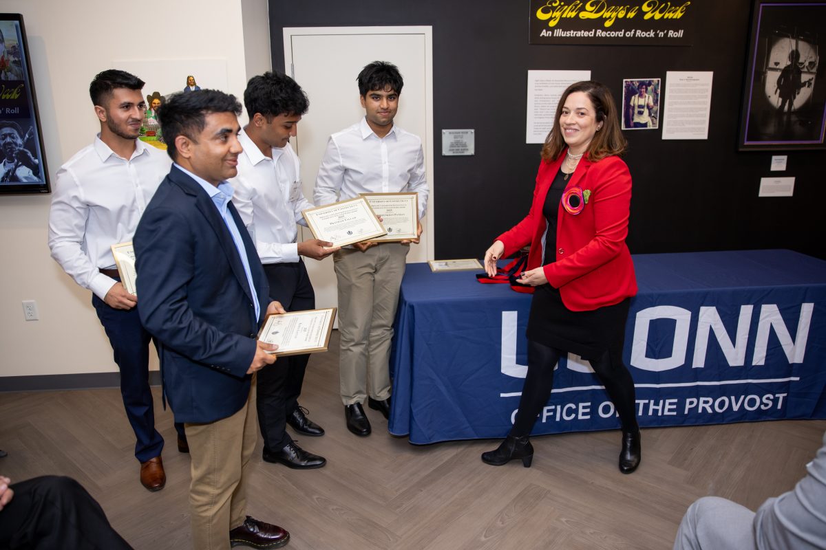 A group of people posing in front of a UConn sign.