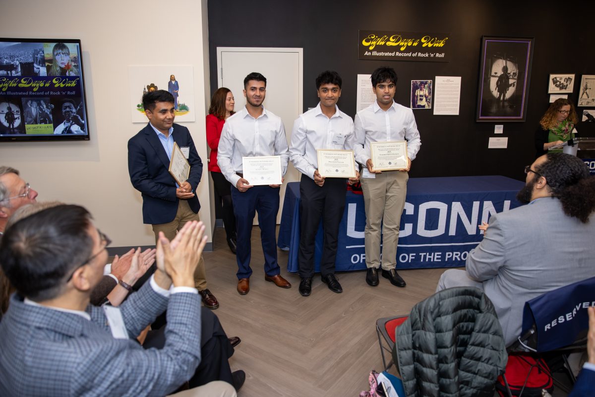 A group of people posing in front of a UConn sign.