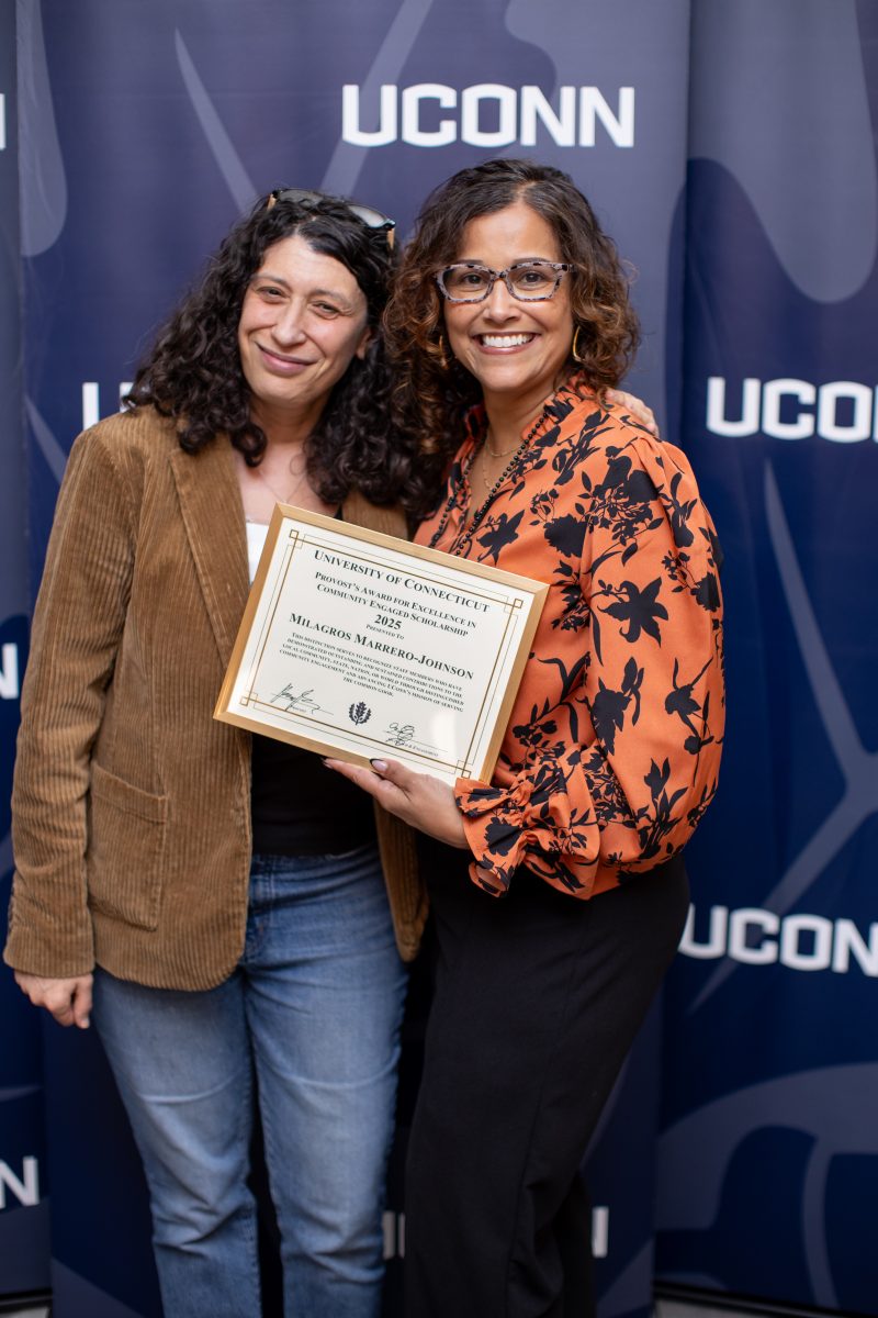 Two people posing in front of a UConn sign.