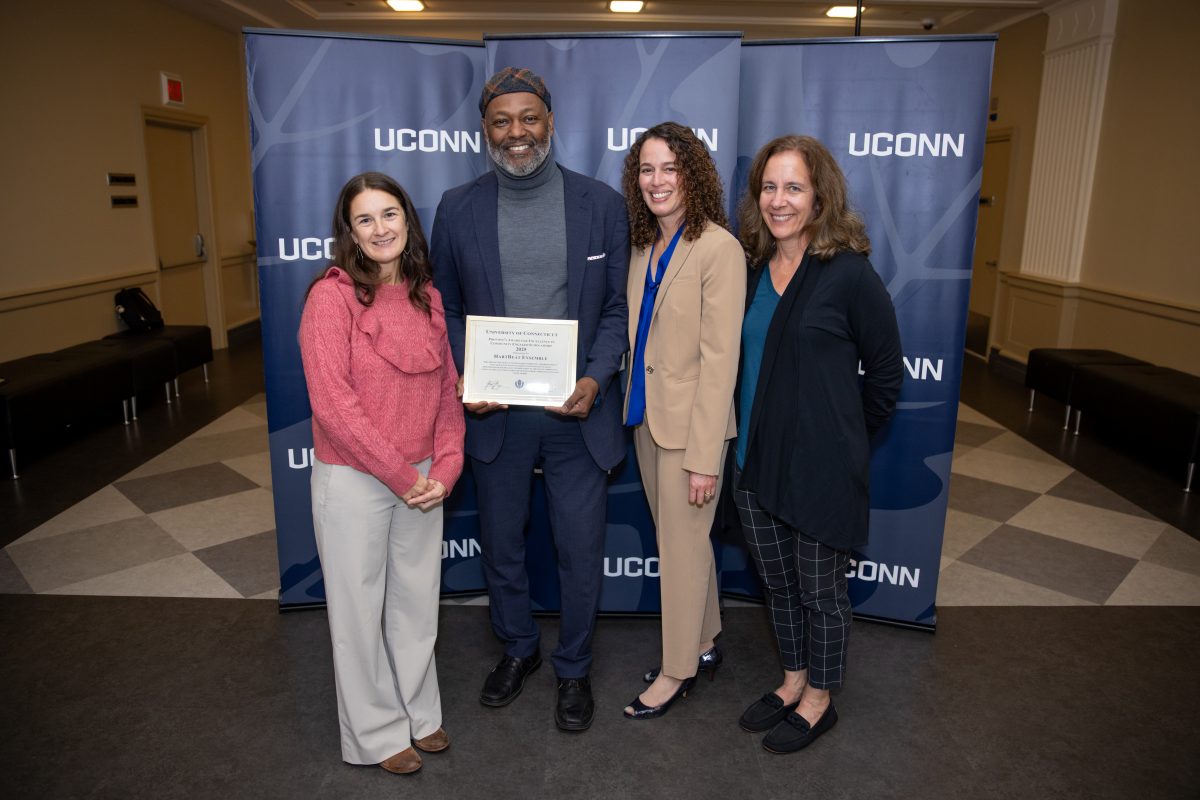 A group of people posing in front of a UConn sign.