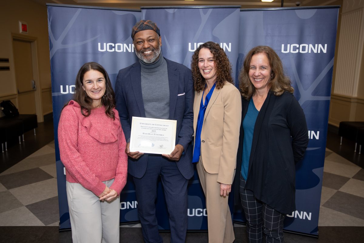A group of people posing in front of a UConn sign.