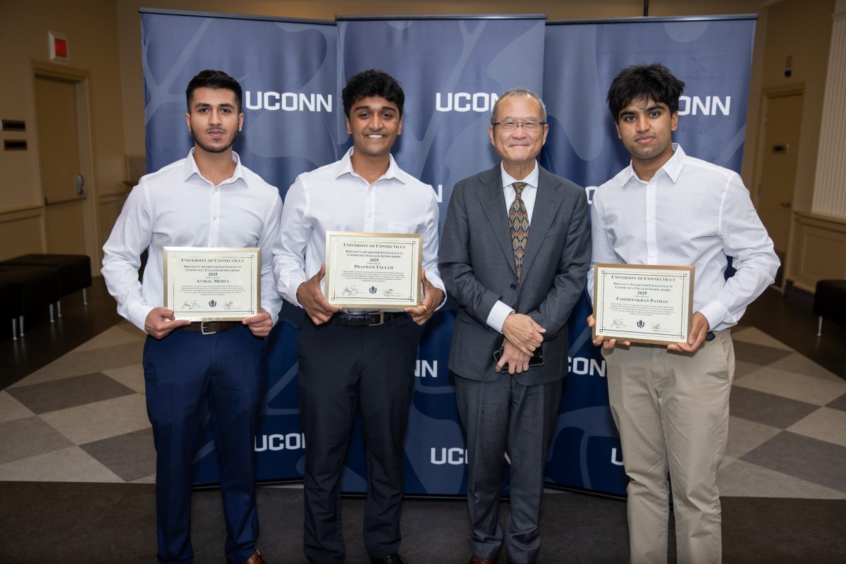 A group of people posing in front of a UConn sign.