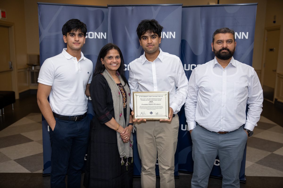 A group of people posing in front of a UConn sign.