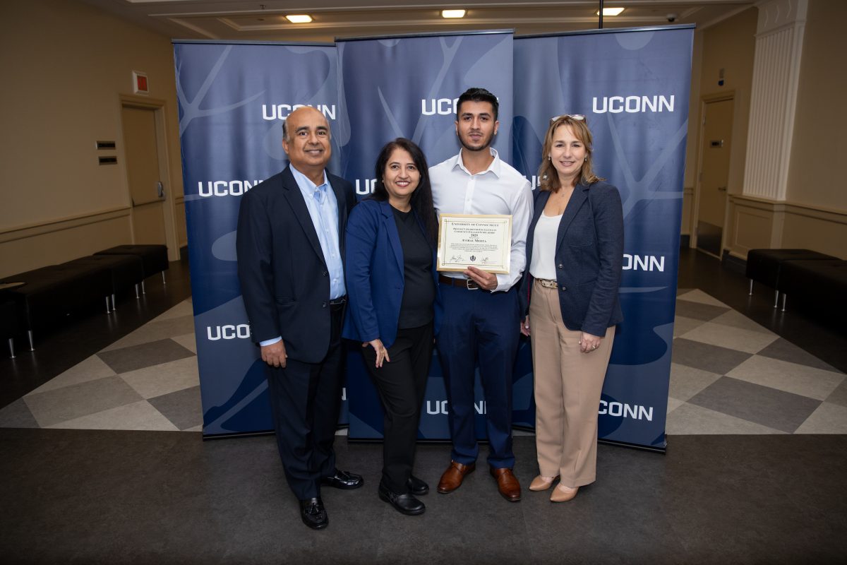 A group of people posing in front of a UConn sign.