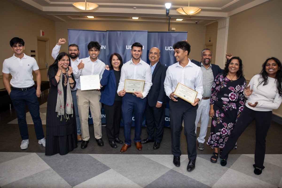 A group of people posing in front of a UConn sign.