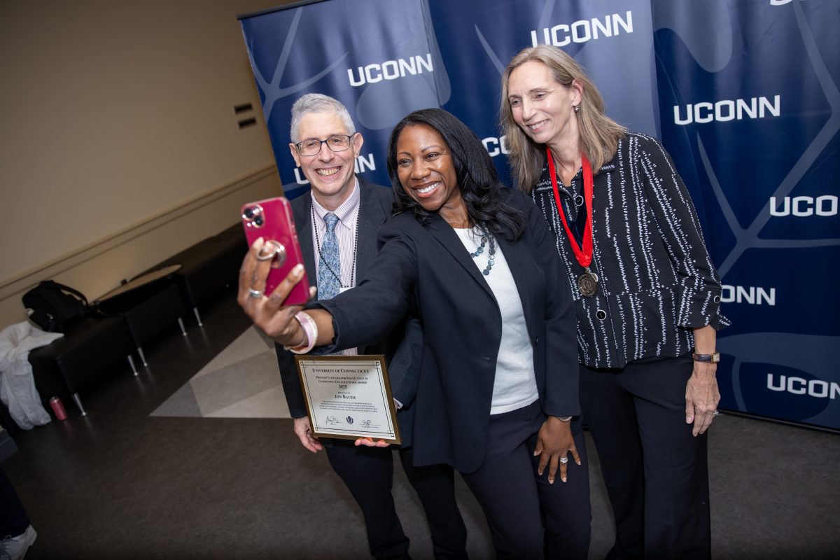 Two people posing for a picture in front of a UConn sign.
