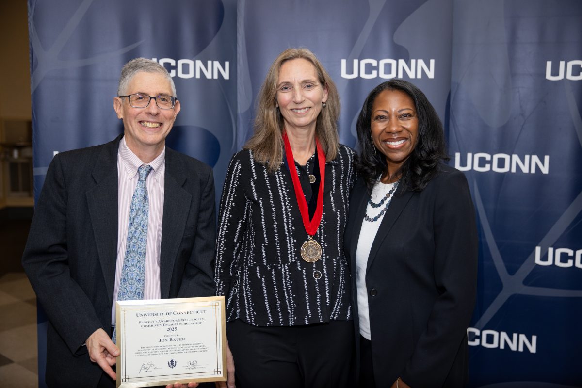 Three people posing for a picture in front of a UConn sign.