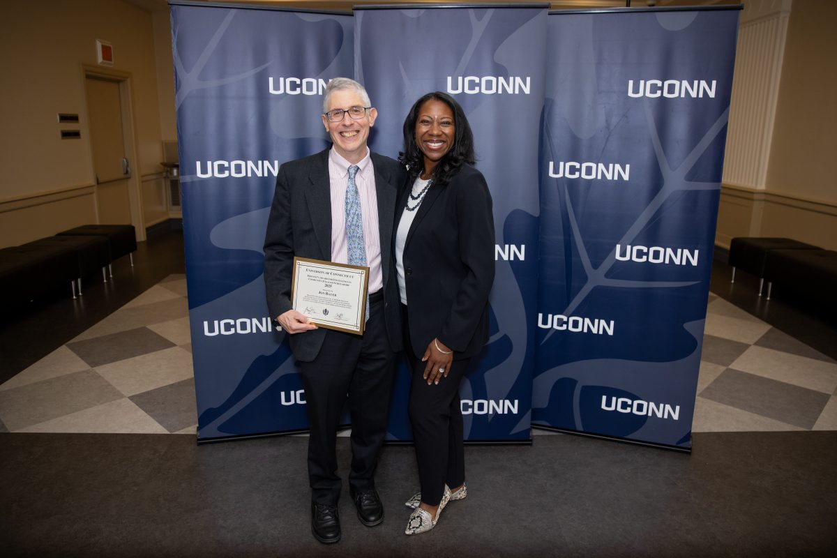 Two people posing for a picture in front of a UConn sign.