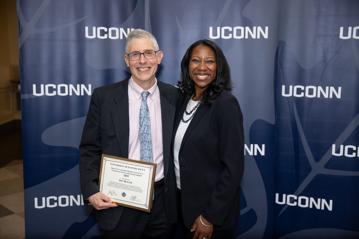 Two people posing for a picture in front of a UConn sign.