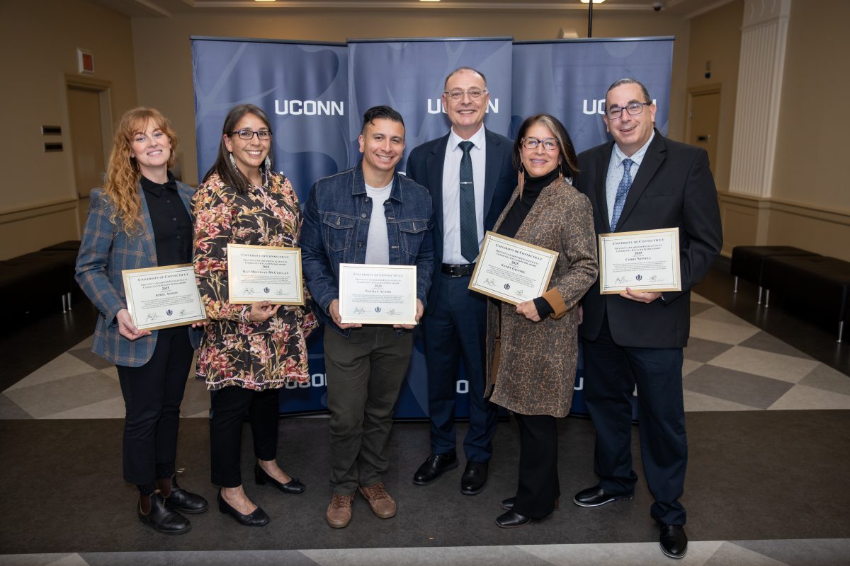 Six people posing for a picture in front of a UConn sign.