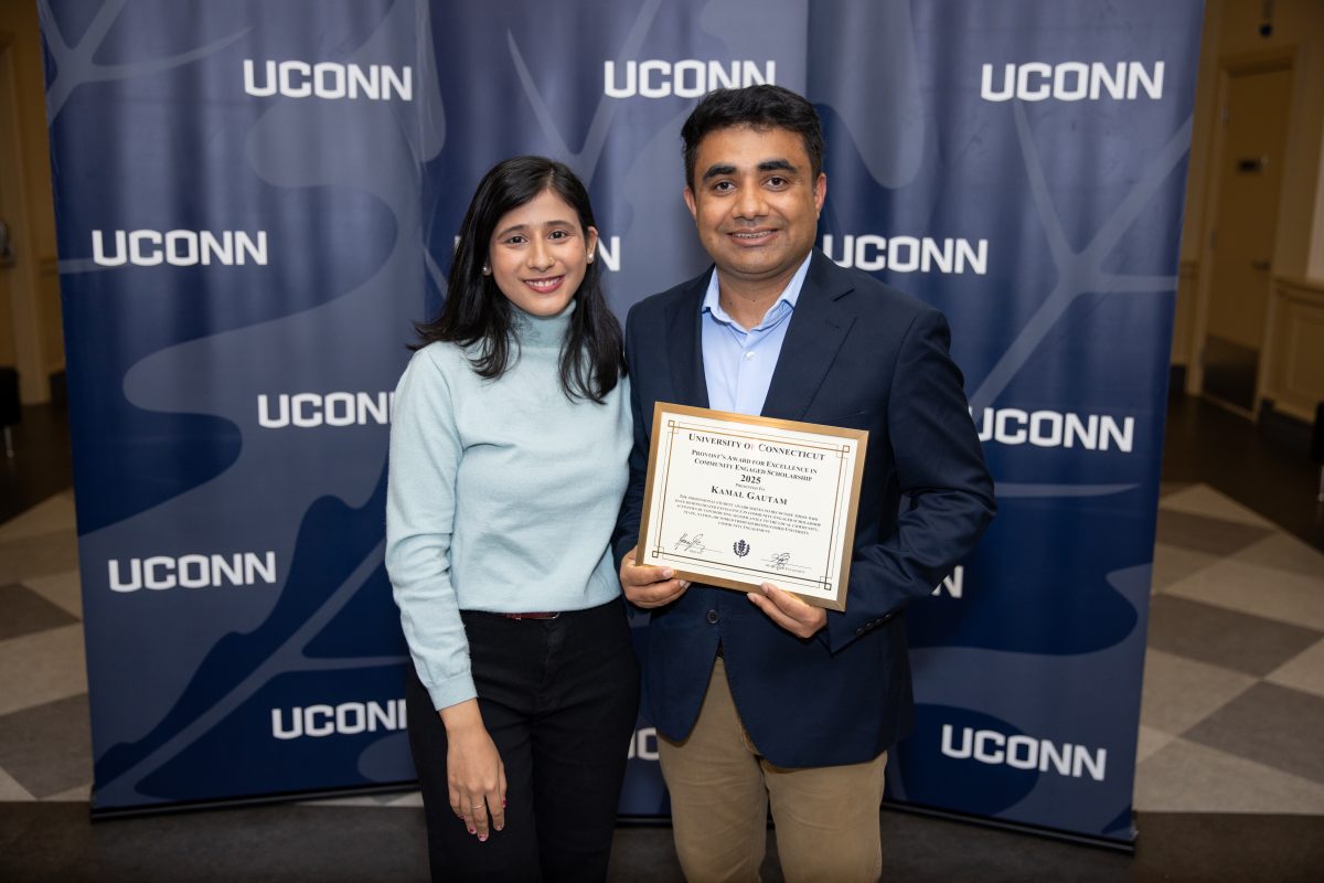 Two people posing for a picture in front of a UConn sign.