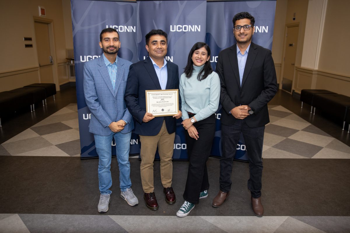 Four people posing for a picture in front of a UConn sign.