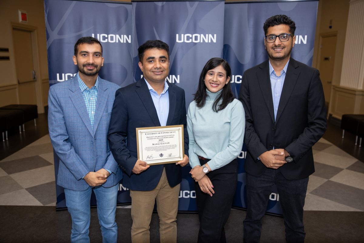 Four people posing for a picture in front of a UConn sign.