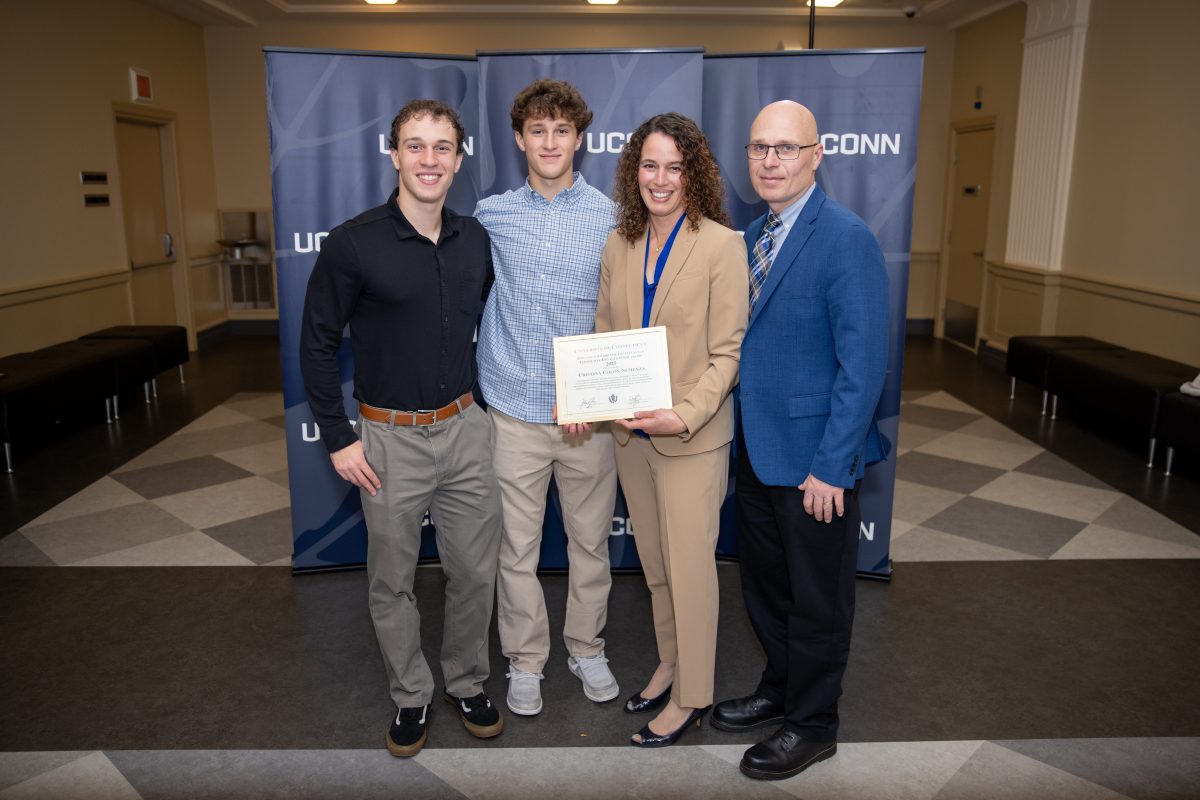 Four people posing for a picture in front of a UConn sign.