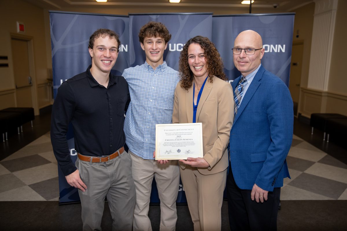 Four people posing for a picture in front of a UConn sign.