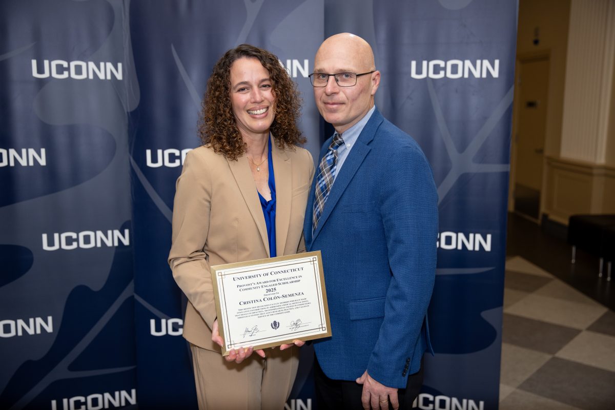 Two people posing for a picture with a UConn sign.