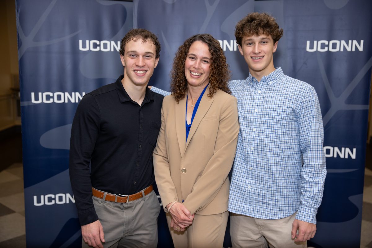 Two gentleman and a lady posing for a picture in front of a UConn sign.