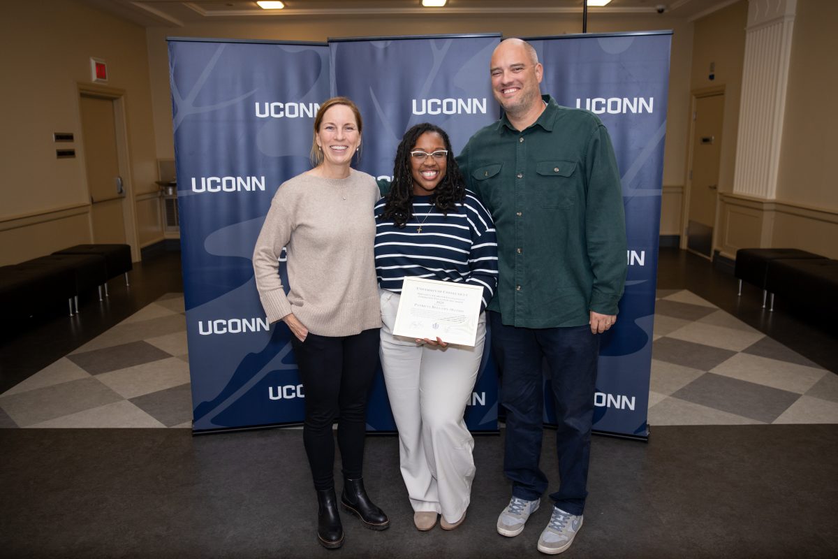 Three people posing for a picture in front of a Uconn sign.