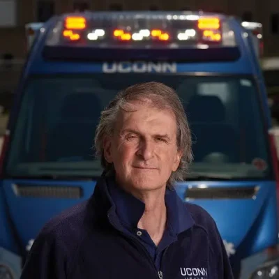 Picture of Peter Canning. He is wearing a stethoscope and in front of an ambulance that says UConn. 